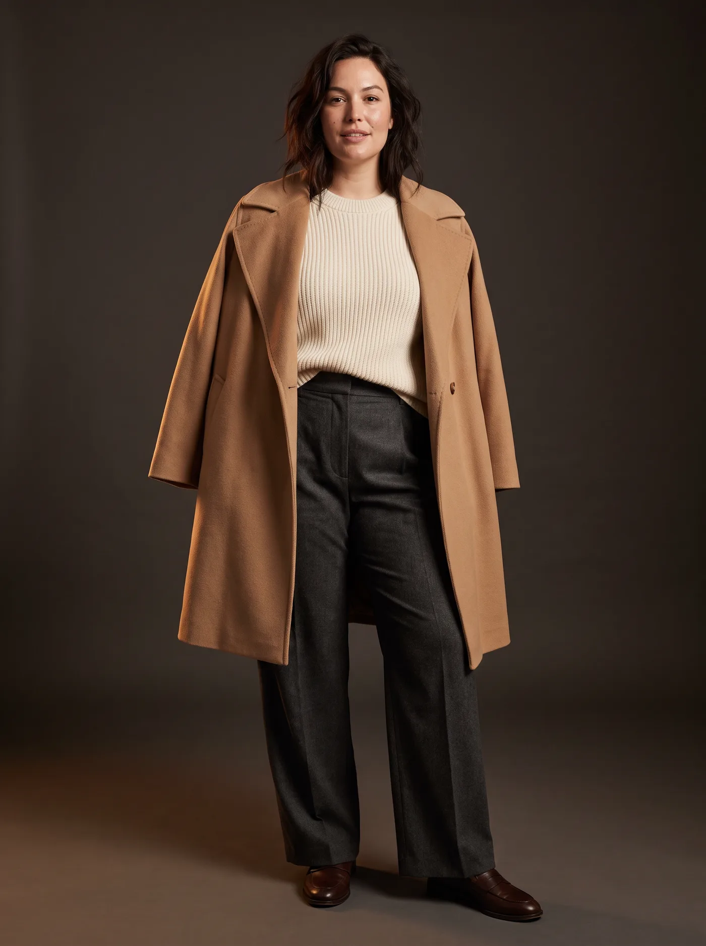A woman wearing a camel coat, cream knit and charcoal trousers from four brands